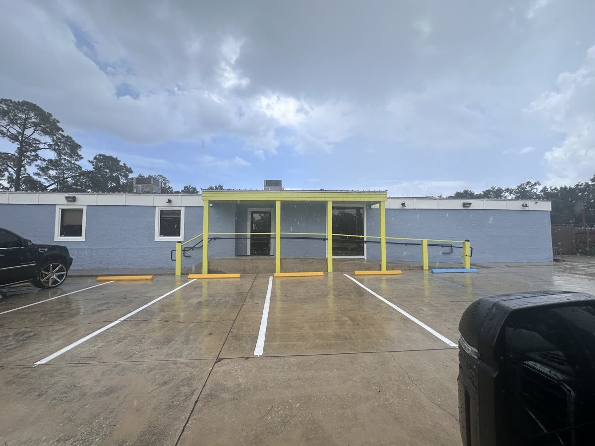The building repainted — fresh blue-gray walls with lime trim and a striped parking lot
